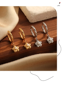 Detailed close-up of gold and silver floral hoop earrings with pearls on dark wood