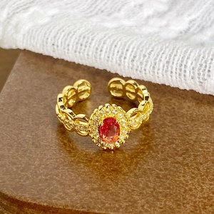Détail d'une bague vintage dorée avec pierre rouge ovale et zircons micro-pavés étincelants