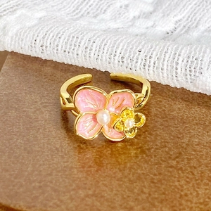 Détail d'une bague dorée vintage avec fleurs en émail rose et étamines en perles