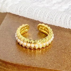 Gros plan sur une bague d'oreille dorée avec perles blanches et reliefs floraux