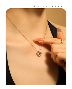 Dettaglio di un ciondolo a quadrifoglio dorato con zirconi a cuore su una collana sottile