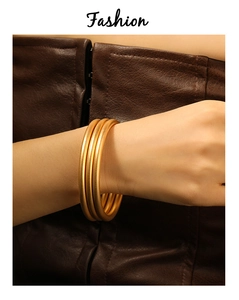 Close-up of three matte gold-plated minimalist bangles on a model's wrist