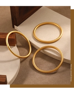 Close-up of three matte 24K gold-plated round bangles on a minimalist wooden display