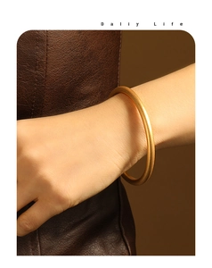 Close-up of a matte gold-plated round bangle bracelet on a woman wrist with leather background