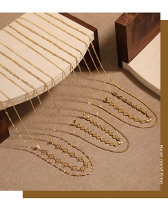 Détail de colliers superposés en plaqué or PVD avec pendentifs cœur et fleur laser
