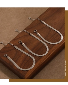Detailed close-up of three flat silver snake chain bracelets with metallic scales on wood