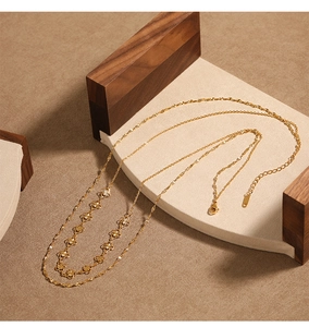 Gros plan d'un collier double épaisseur doré avec breloques fleurs sur support bois