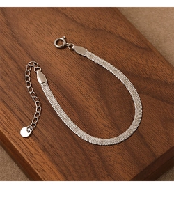 Detailed close-up of a silver flat snake bone chain with an adjustable clasp on dark wood