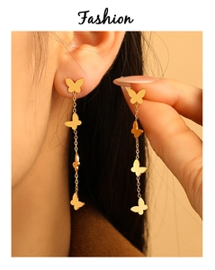 Detalle de pendientes de borla dorados con dijes de mariposas en cascada