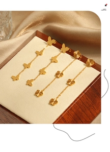 Detalle de pendientes de cadena dorada con trébol de cuatro hojas y borla de mariposa