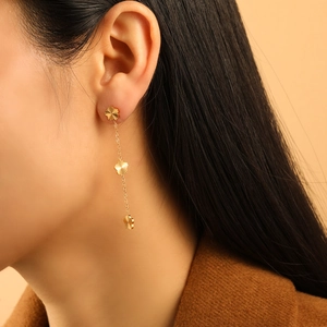 Elegantes pendientes de trébol de acero de titanio dorado en una modelo femenina