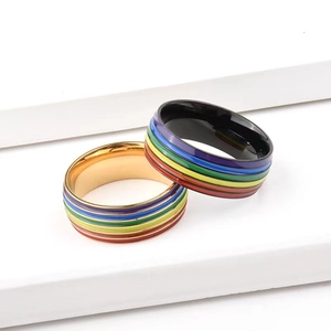 Rainbow striped titanium steel rings in gold and black finishes on a white geometric stand