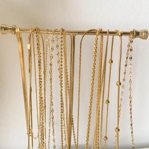 Collection of various 24K gold plated titanium steel necklaces on T-bar metal stand