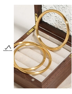 Three-piece set of polished golden stainless steel bangles in a vintage wooden jewelry box