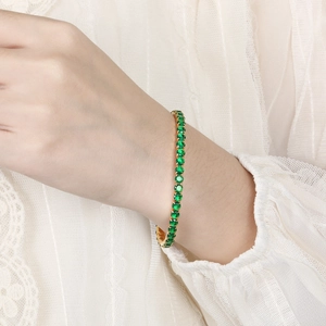 Elegant gold tennis bracelet with emerald green zircon crystals on a lace background