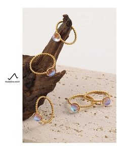 Detalle de anillos de acero inoxidable dorado trenzado con piedras de luna iridiscentes