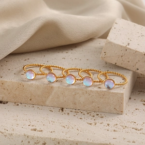 Set de cinco anillos dorados de cuerda con piedras de luna arcoíris sobre fondo piedra