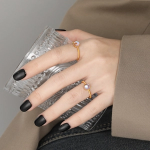 Anillo dorado trenzado con piedra lunar usado por modelo con copa de vidrio