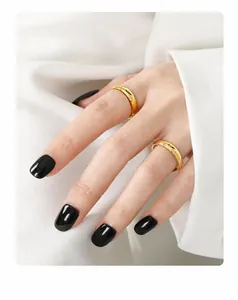 Primer plano de dos anillos de titanio dorado pulido en modelo con esmalte de uñas negro