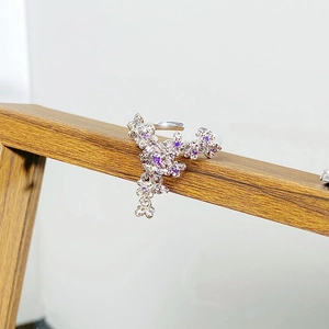Detail of silver floral ring with purple zircon petals and hanging charm on wood stand
