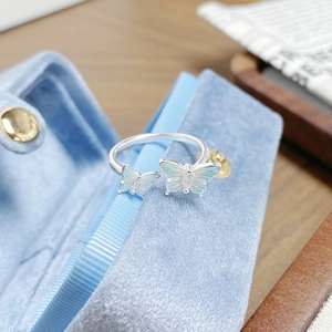 Détail de deux papillons en émail bleu sur une bague ajustable en argent dans son écrin