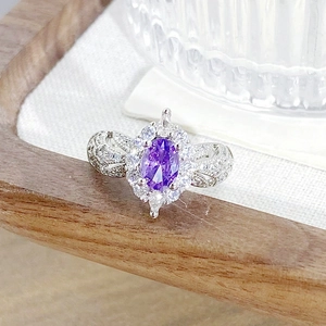 Detailed close-up of a silver ring with oval purple gemstone and crystal pavé accents
