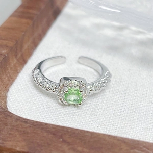 Close-up of square green gemstone ring with pavé diamonds on an adjustable band