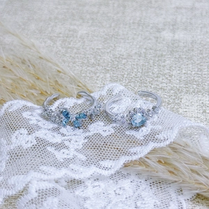 Detailed macro of silver butterfly and flower open rings with light blue gemstones on lace