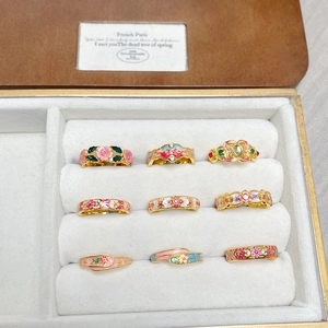 Detailed top view of nine vintage floral enamel rings with crystals in a jewelry box