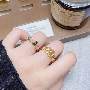 Close-up of vintage gold rings with pink enamel flower and gemstones on woman hand