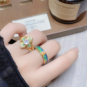 Close-up of vintage gold flower and colorful enamel rings worn on fingers in a retro setting
