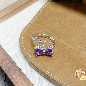 Close-up of silver bow ring with purple heart-shaped zircons on brown velvet