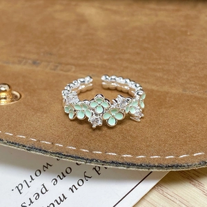 Détail macro d'une bague réglable argentée avec fleurs en émail vert menthe et zircon