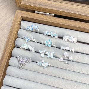 Close-up of floral enamel rings with butterfly motifs in a grey velvet jewelry display box