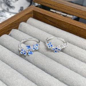 Detail shot of two blue enamel flower rings with zircon accents in a wooden jewelry box