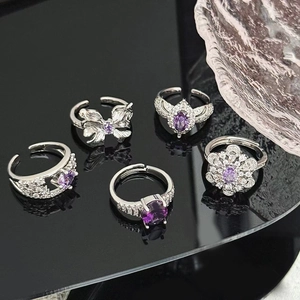 Macro detail of five silver rings with purple zircons and diamond accents on black surface