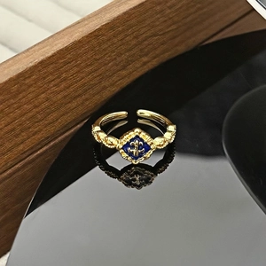 Detailaufnahme eines Vintage-Goldrings mit blauem Emaille-Lilien-Muster auf schwarzer Fläche