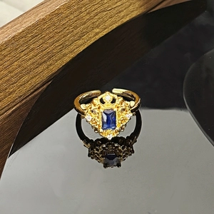 Makroaufnahme eines Vintage-Goldrings mit blauem Edelstein auf schwarzer Spiegelfläche