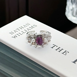 Detail of silver textured ring with oval purple gemstone and side pearls on a book
