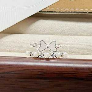 Macro detail of silver-tone enamel bow ring paired with a sparkling pearl band set