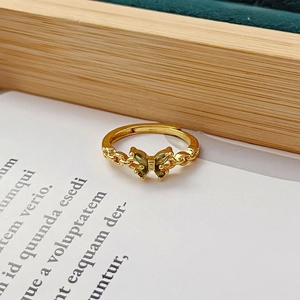 Détail de bague papillon dorée avec pierres vertes sur un socle en velours vert