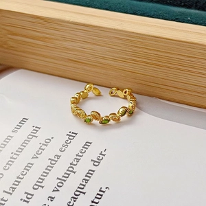 Vue détaillée de la bague feuille dorée avec gemmes vertes sur papier vintage
