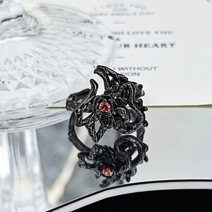 Macro detail of gothic black spider ring with faceted red gemstone on mirror surface