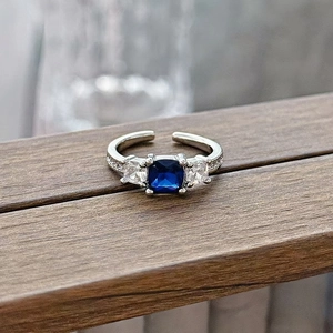 Close-up of square blue gemstone ring with small zircons on a rustic wood surface