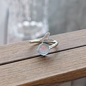 Close-up of mermaid tail open ring with iridescent gemstone on natural wood texture