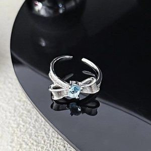 Detailed macro view of silver bow ring with blue oval gemstone on black reflective surface