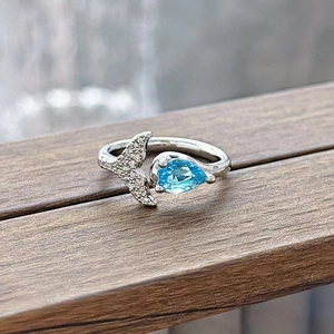 Close-up of sea blue pear-cut gemstone and sparkling fish tail detail on silver ring