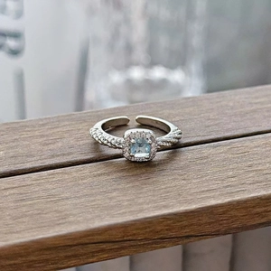 Close-up of aquamarine blue gemstone ring with halo diamonds on a rustic wooden surface