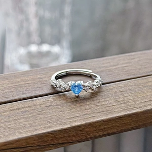Macro shot of a heart-shaped blue zircon ring with small side diamonds on a wooden surface