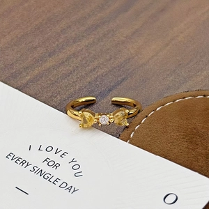 Goldener Schleifenring mit gelben Herzsteinen und verstellbarem Band auf Holzständer